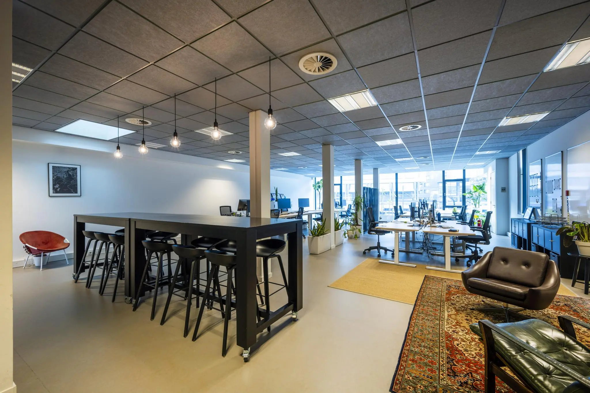 Moderne en open kantoorruimte aan de De Ruijterkade met werkplekken, hoge tafel met barkrukken en een loungehoek.