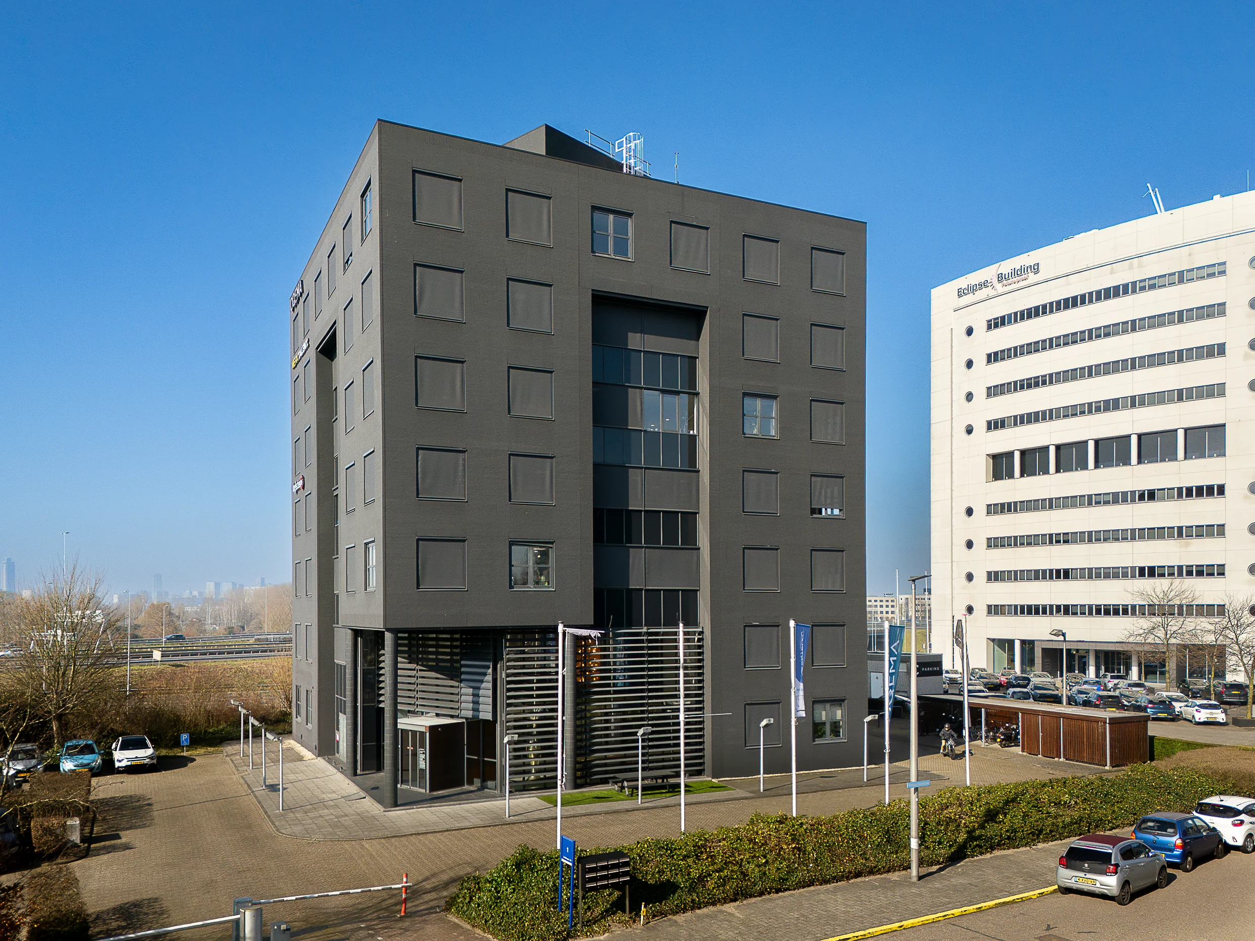 Modern black office building at Rivium Quadrant in Capelle aan den IJssel, with clear blue sky and parked cars in front.