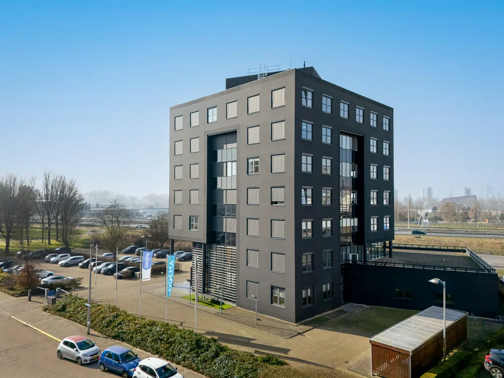 Modern black office building at Rivium Quadrant with adjacent parking lot and city skyline in the background.