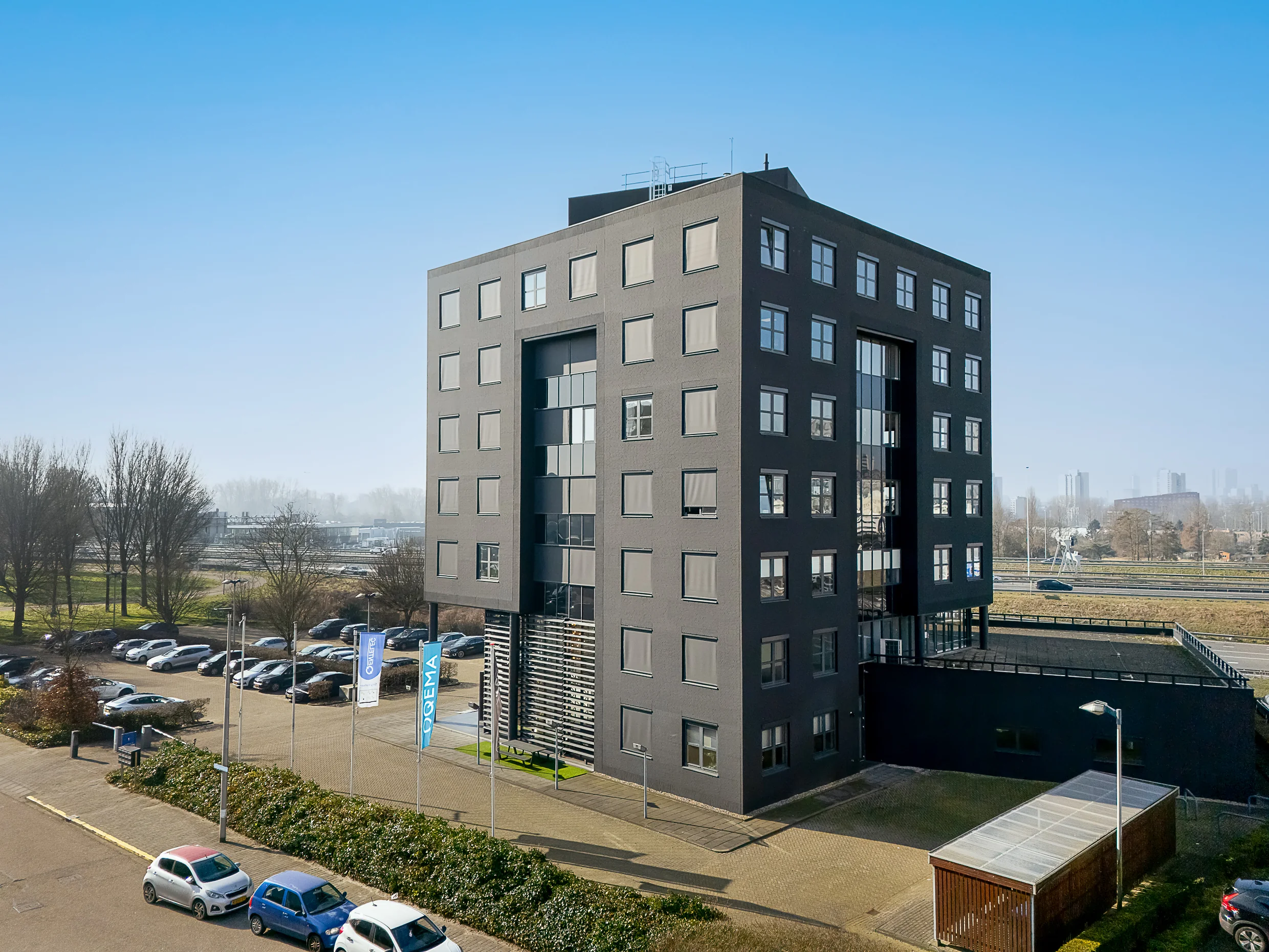 Modern black office building at Rivium Quadrant with adjacent parking lot and city skyline in the background.