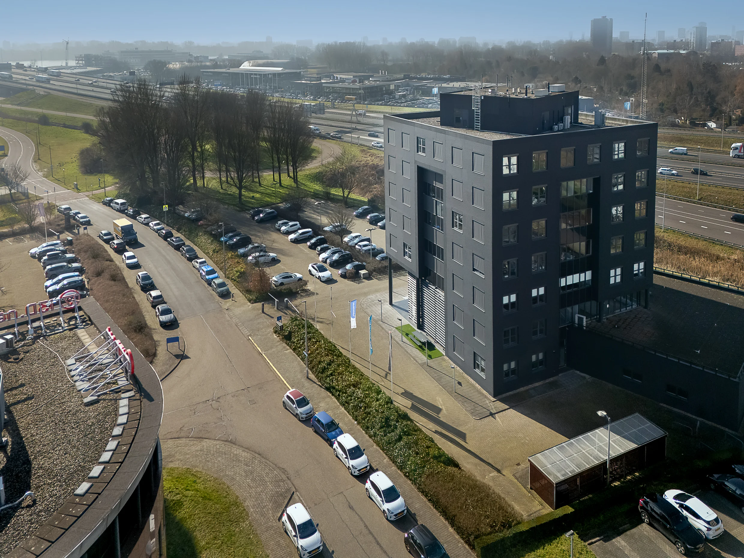 Modern office building at Rivium Quadrant with adjacent parking lot and nearby highway in a business district.