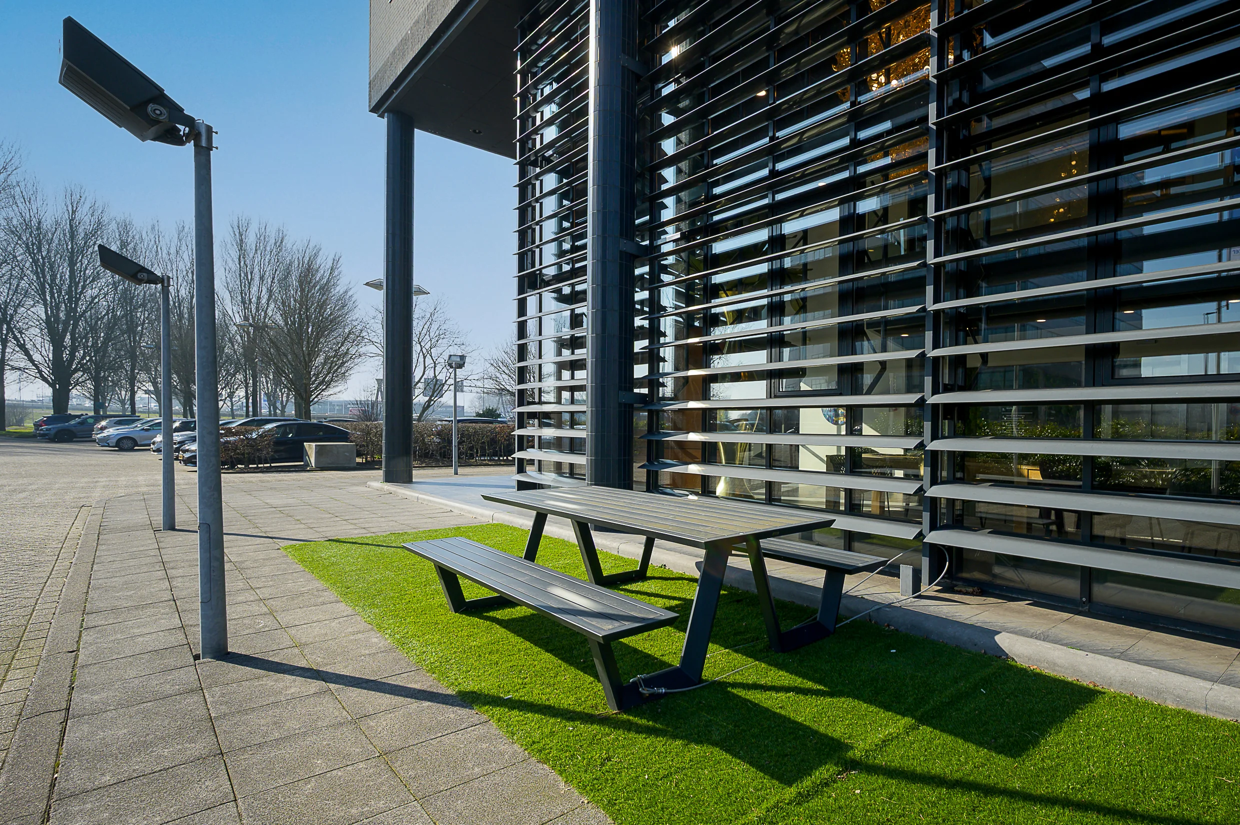 Modern office building at Rivium Quadrant with outdoor seating area on artificial grass near a parking lot.