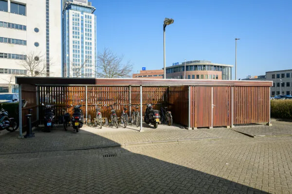 Covered bicycle and scooter parking area at Rivium Quadrant with office buildings in the background.