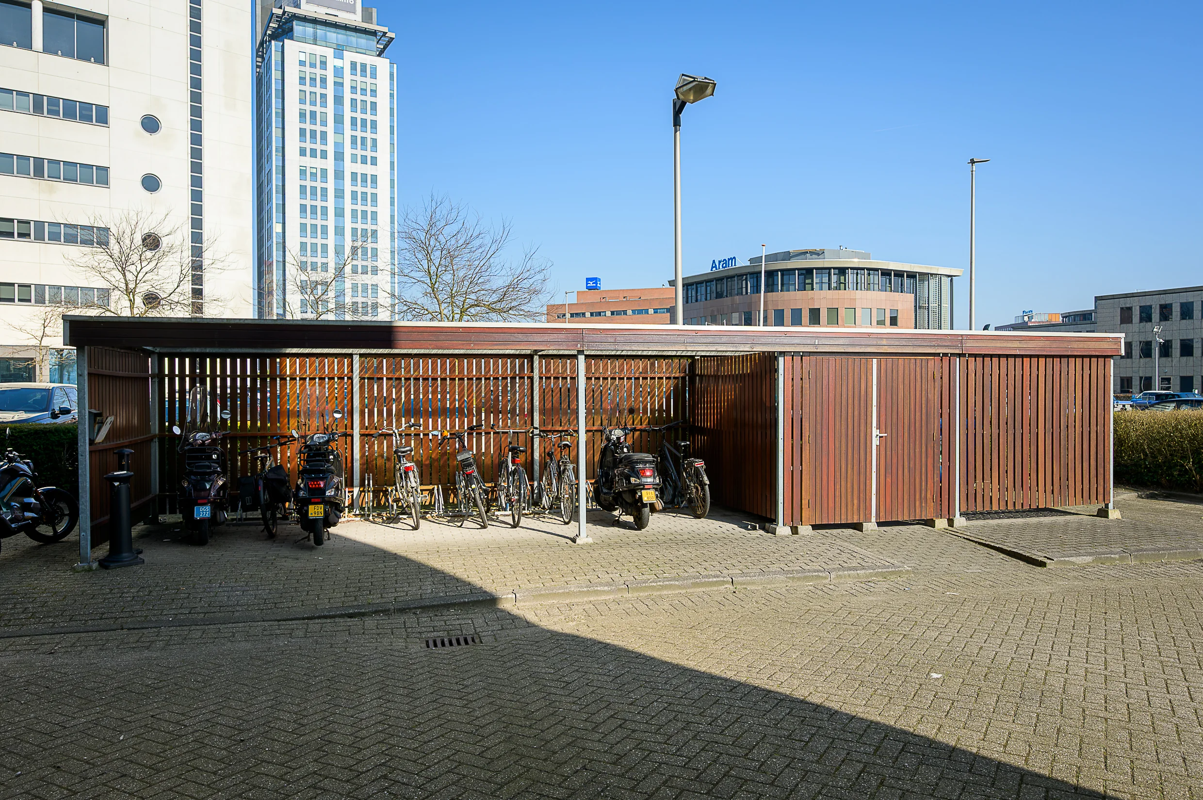 Covered bicycle and scooter parking area at Rivium Quadrant with office buildings in the background.