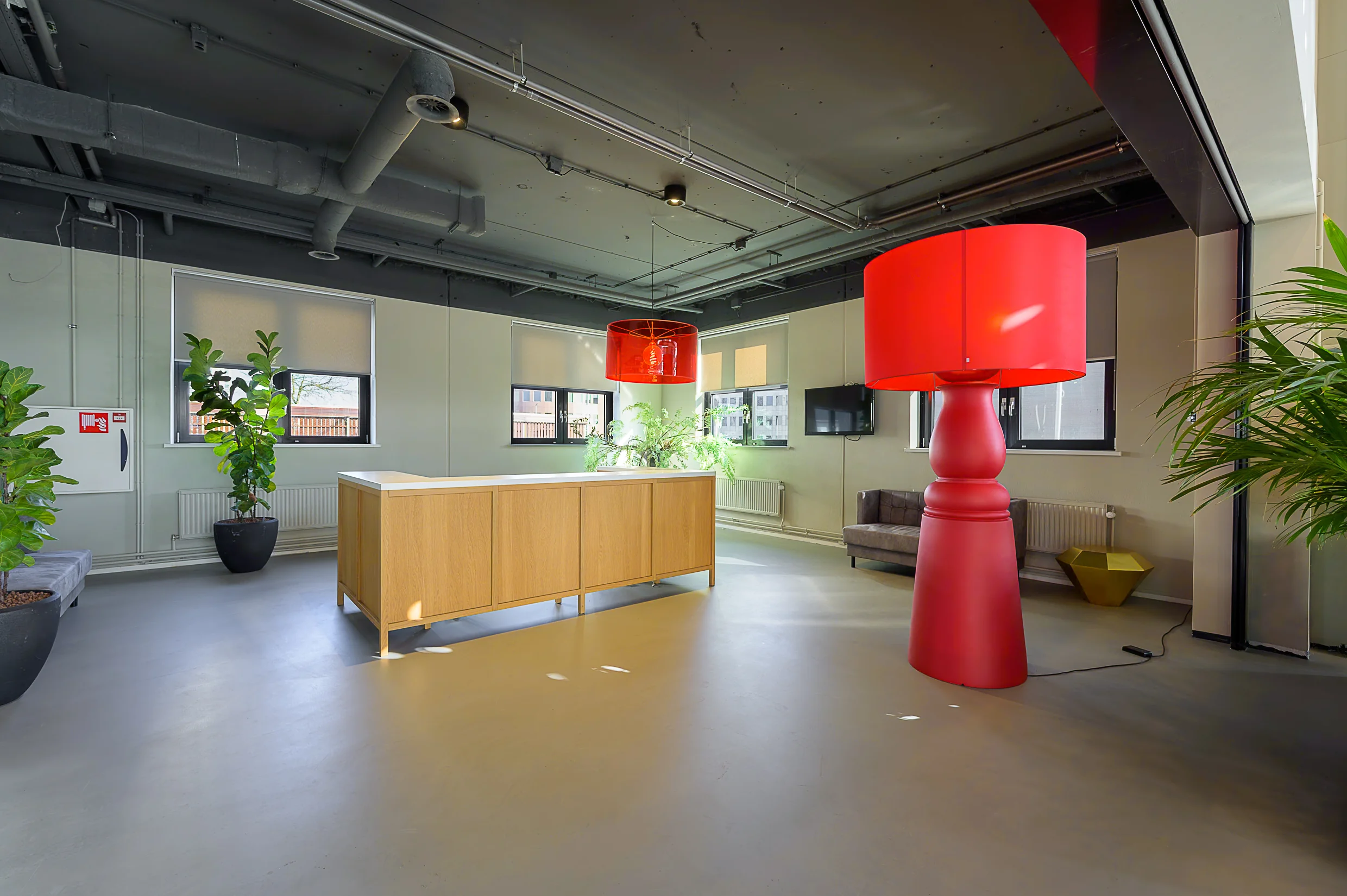 Modern office lobby at Rivium Quadrant with large red lamps, indoor plants, and a wooden reception desk.