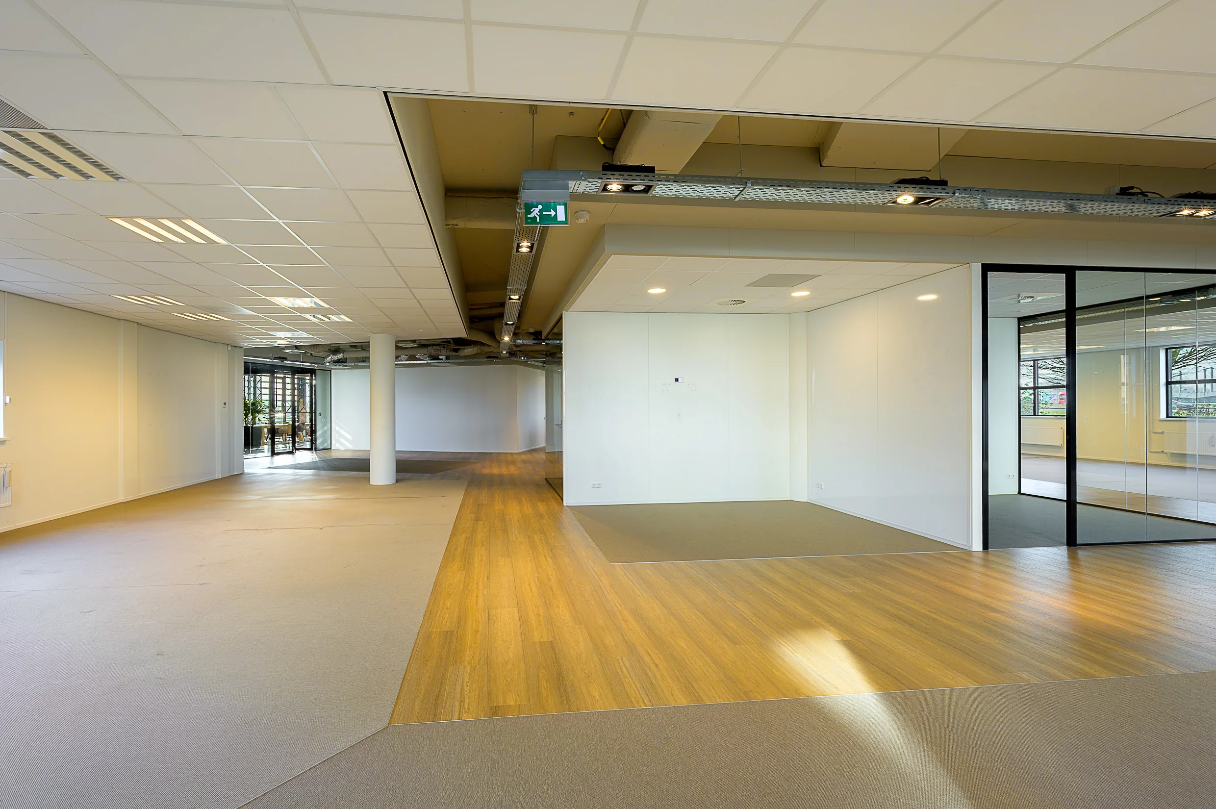 Modern empty office space at Rivium Quadrant with mixed flooring, white walls, and glass partition.