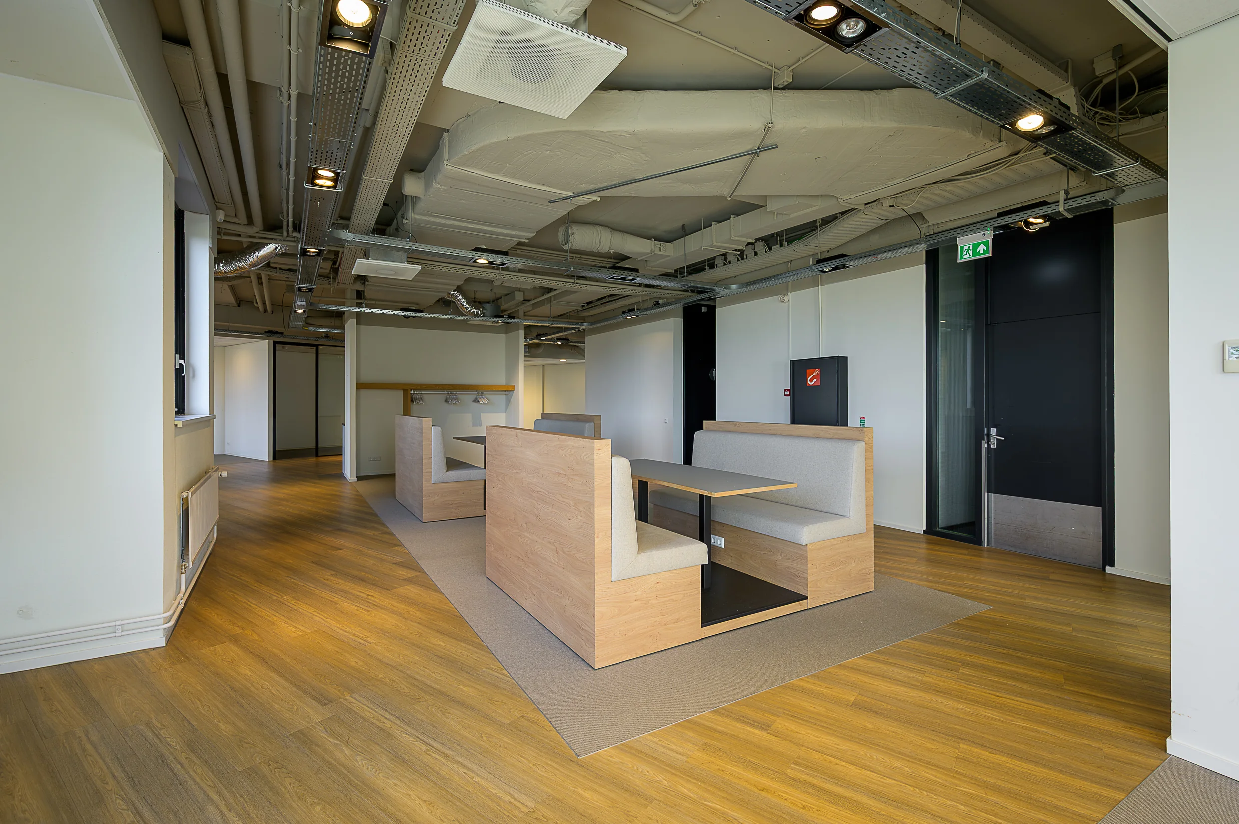 Modern office seating area at Rivium Quadrant with wooden booths and exposed ceiling infrastructure.