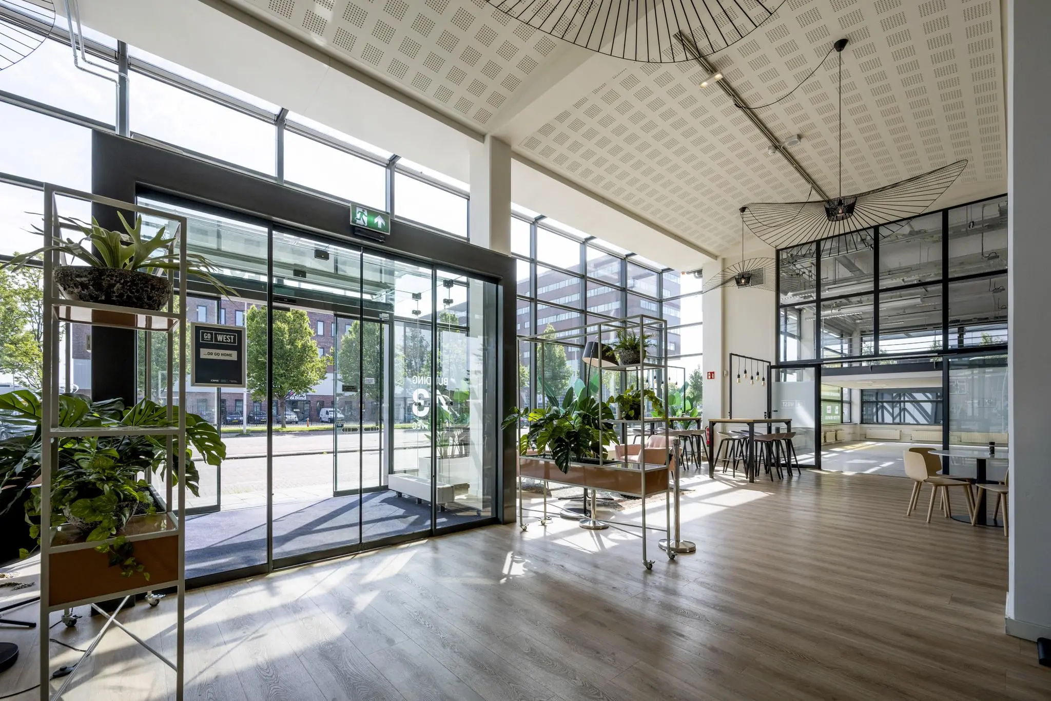 Moderne, lichte entreehal van een kantoorgebouw aan de Kabelweg met glazen gevel, planten en zithoeken.