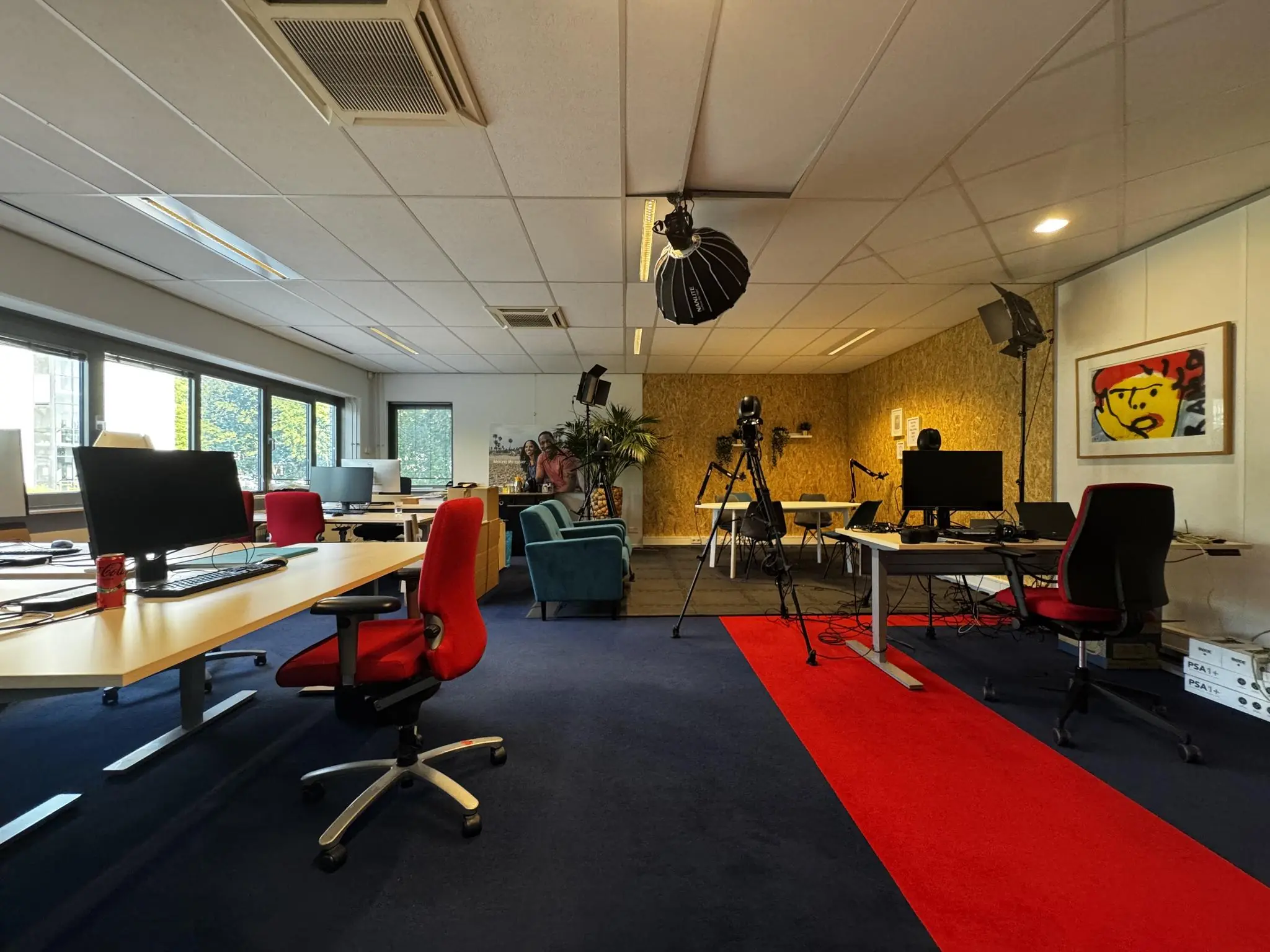 Moderne kantoorruimte aan de Softwareweg met werkplekken, studioapparatuur en een rode loper op donkerblauw tapijt.