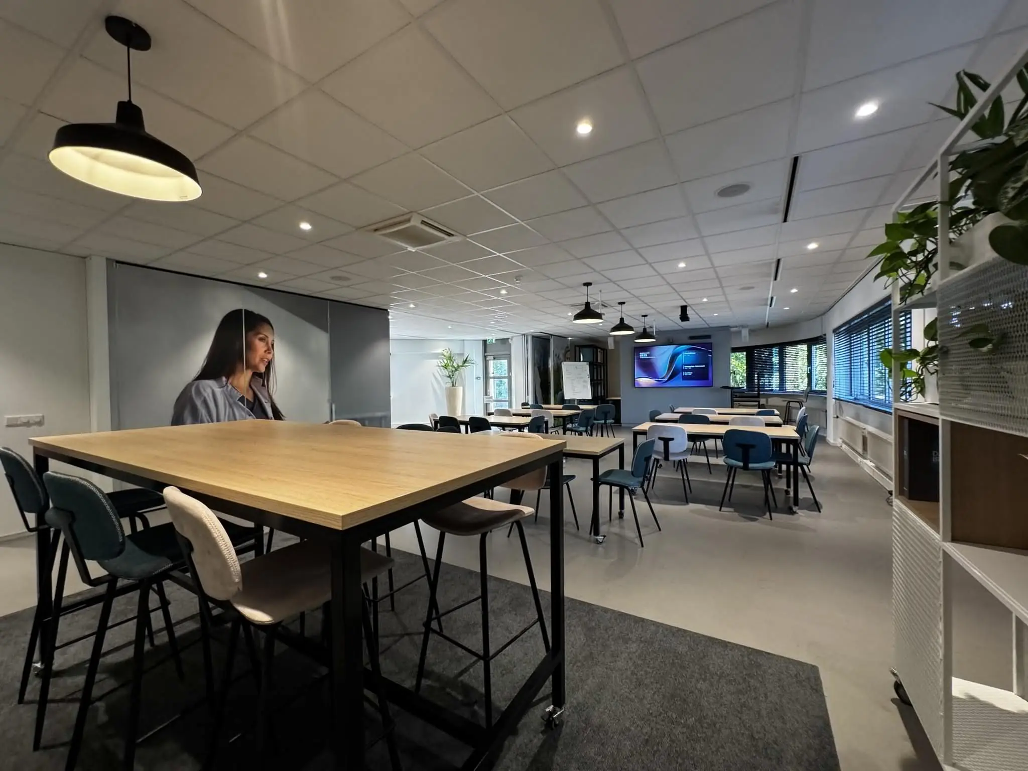 Moderne en ruim ingerichte kantoorlunchruimte of vergaderruimte aan de Softwareweg, met diverse zitplaatsen, planten en een groot scherm.
