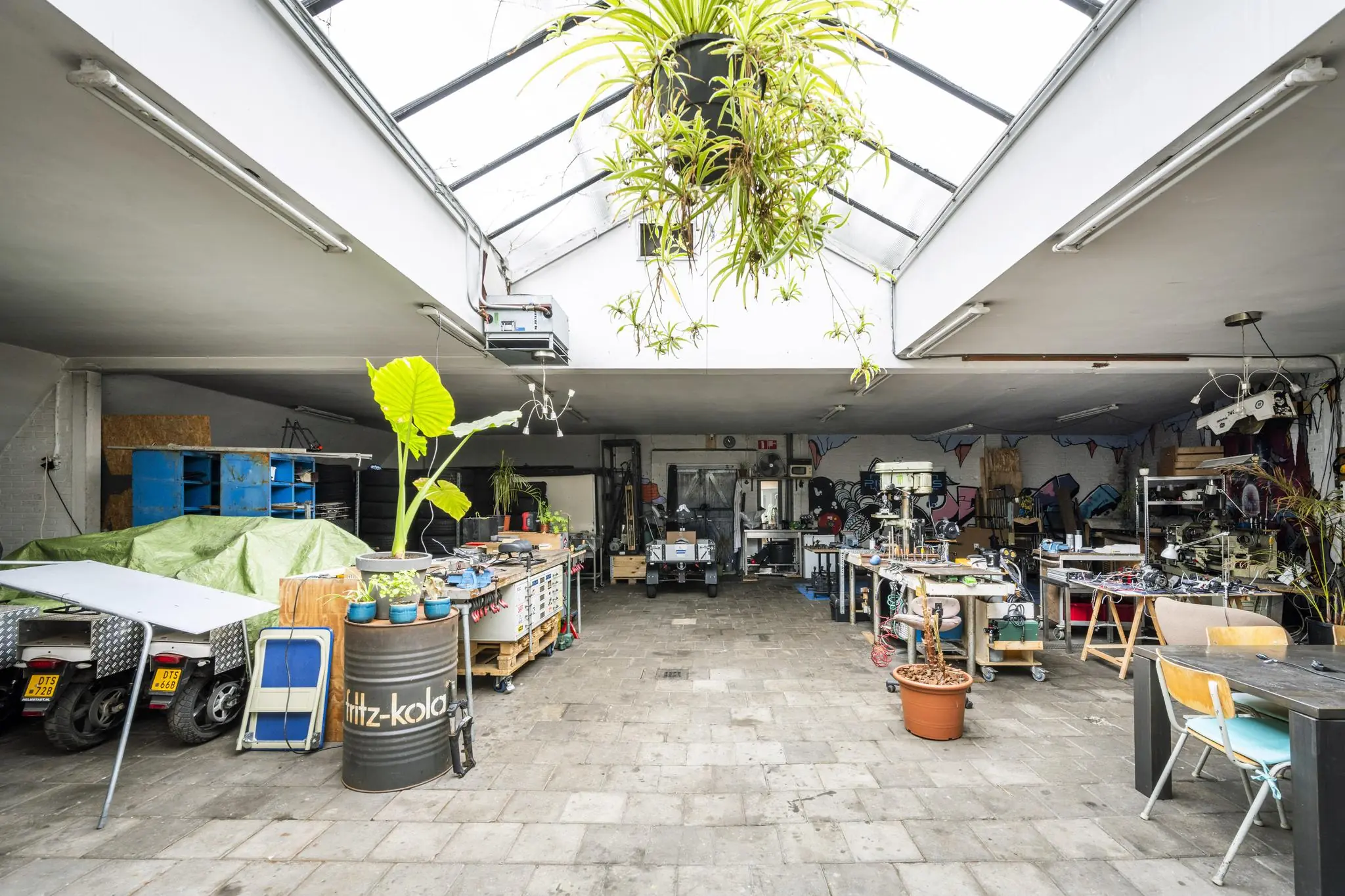 Ruimtelijke en lichte werkplaats aan de Baarsjesweg met werkbanken, gereedschap, planten en een industriële sfeer.