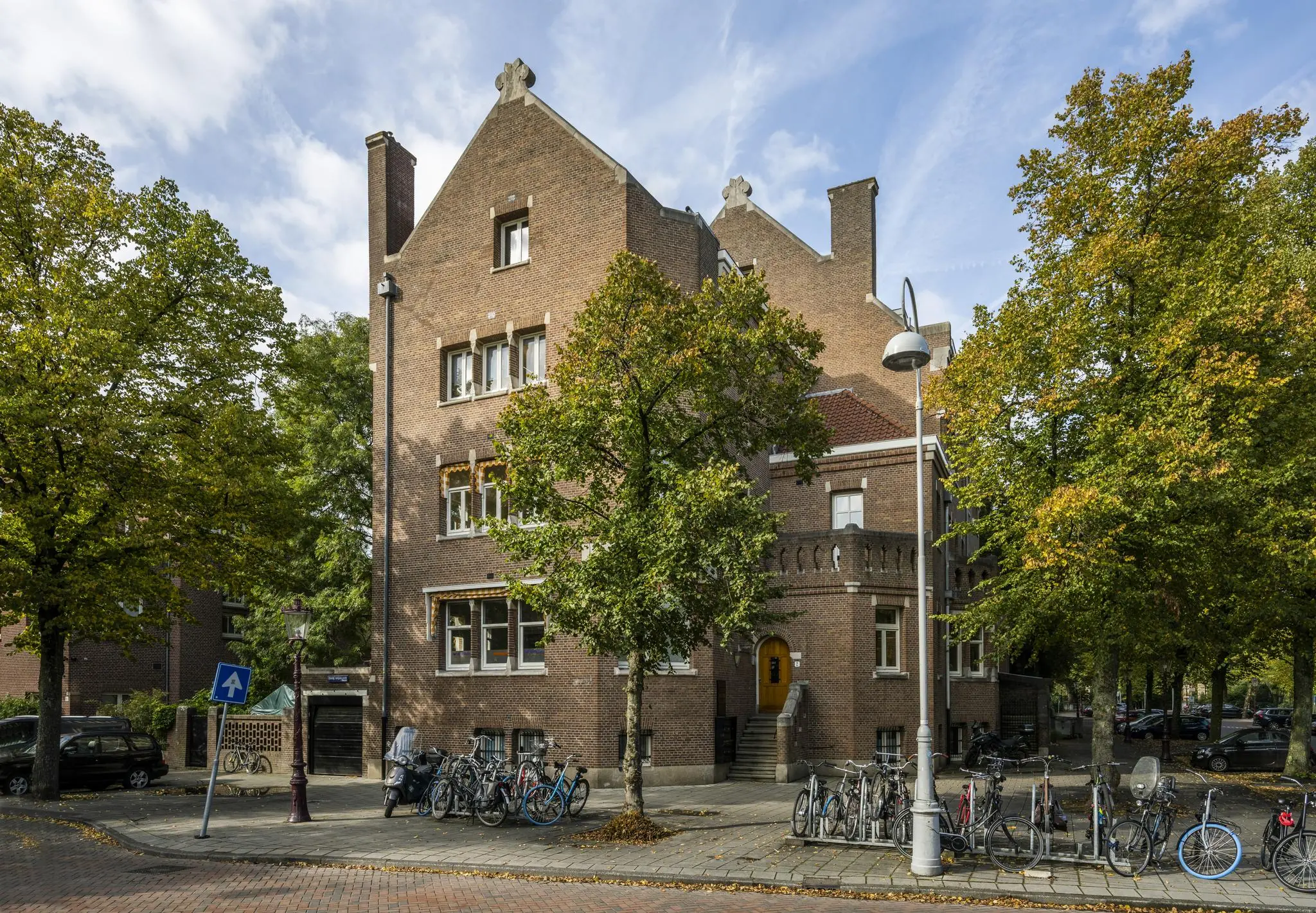 Monumentaal bakstenen pand aan het Emmaplein in Amsterdam, omringd door bomen en geparkeerde fietsen.