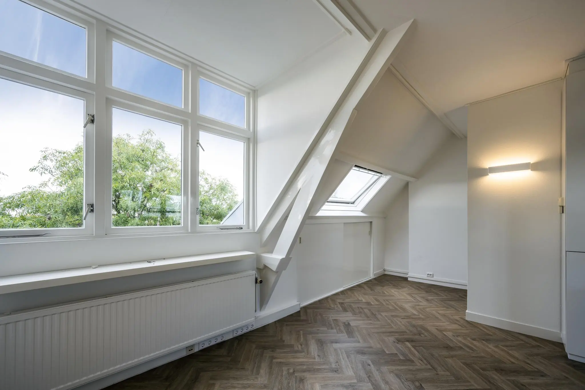 Lichte zolderkamer aan het Emmaplein met een groot raam, dakraam en visgraatvloer.