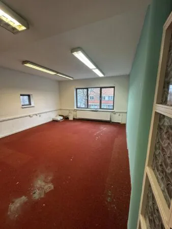 Lege kamer met rood tapijt, witte muren en een groot raam met uitzicht op de Nassaulaan.