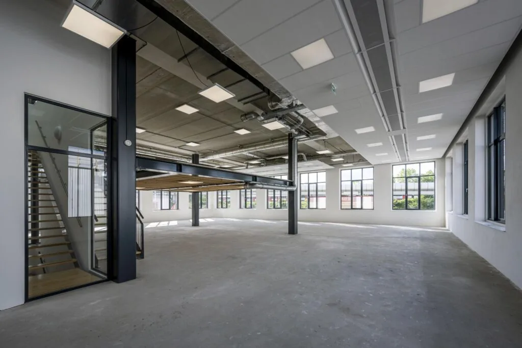 Moderne, lege kantoorruimte aan de Nicolaas Tetterodestraat met grote ramen, betonnen vloer en een metalen tussenverdieping.