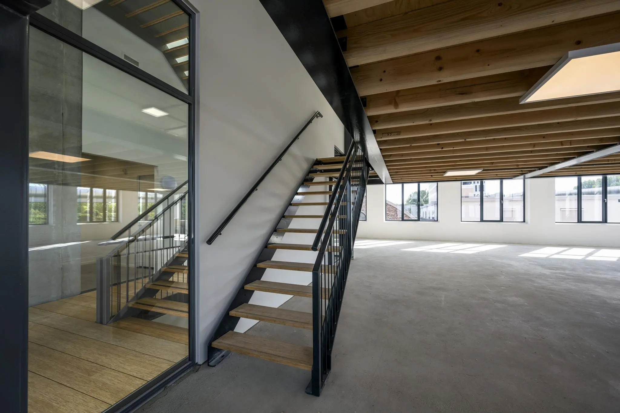 Interieur van een lege, moderne kantoorruimte aan de Nicolaas Tetterodestraat met een open trap, betonnen vloer en houten plafondbalken.