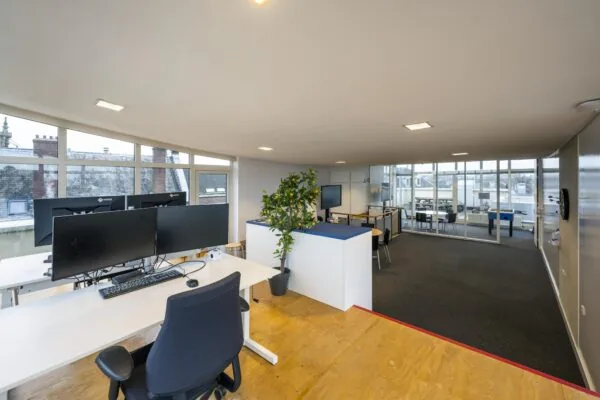 Moderne kantoorruimte aan de Prins Hendrikkade met werkplekken, vergaderruimte en grote ramen met uitzicht op oude daken.