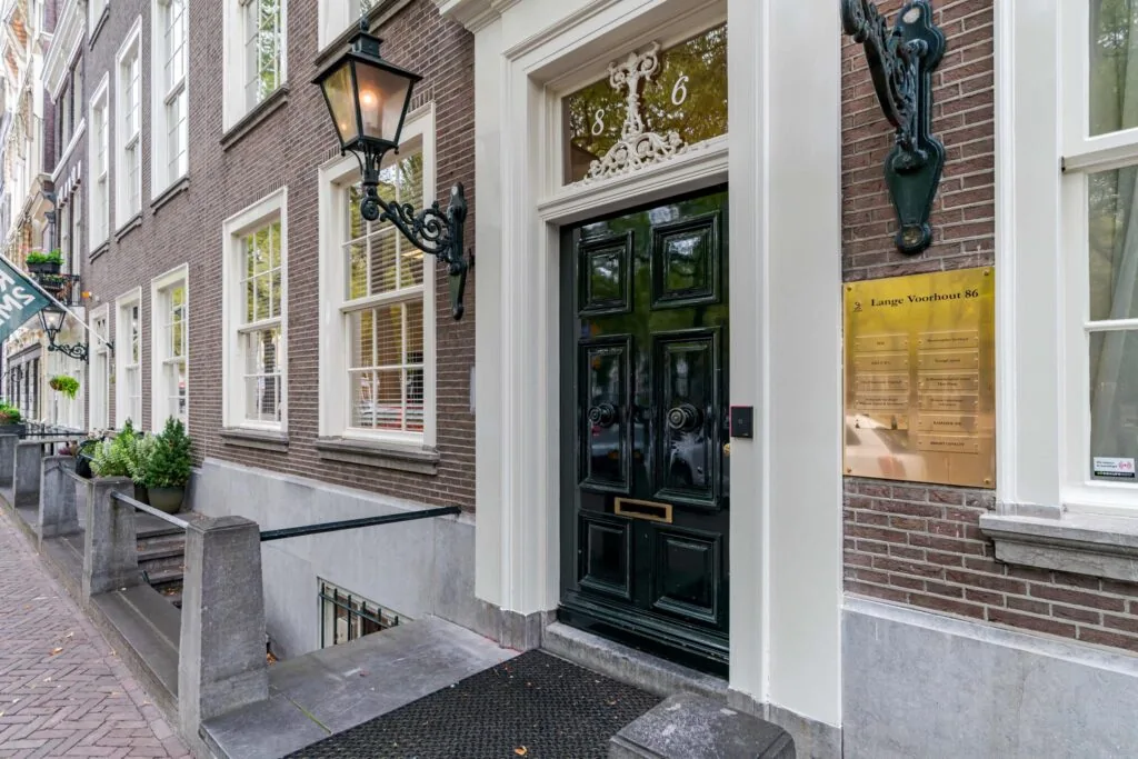 Ingang van een klassiek herenhuis aan Lange Voorhout 86 met zwarte voordeur, gevelbord en smeedijzeren lantaarns.