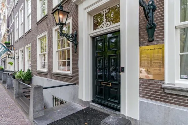 Ingang van een klassiek herenhuis aan Lange Voorhout 86 met zwarte voordeur, gevelbord en smeedijzeren lantaarns.
