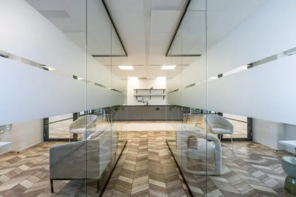 Moderne kantoorpauzeruimte aan de Overschiestraat met glazen wanden, houten visgraatvloer en minimalistisch interieur.