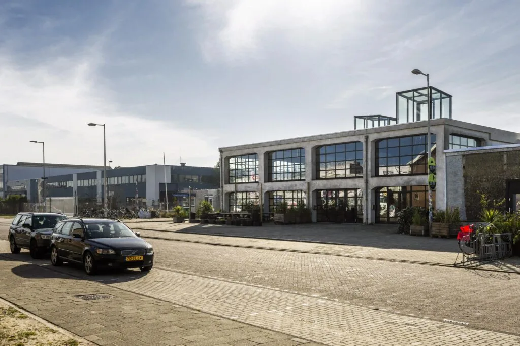 Industrieel pand aan het Gedempt Hamerkanaal met grote ramen en geparkeerde auto's op de voorgrond.