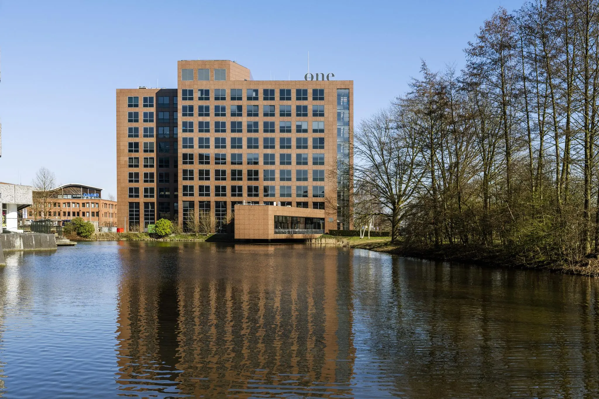 Kantoorgebouw aan de Prof. W.H. Keesomlaan, weerspiegeld in het water met bomen op de achtergrond.