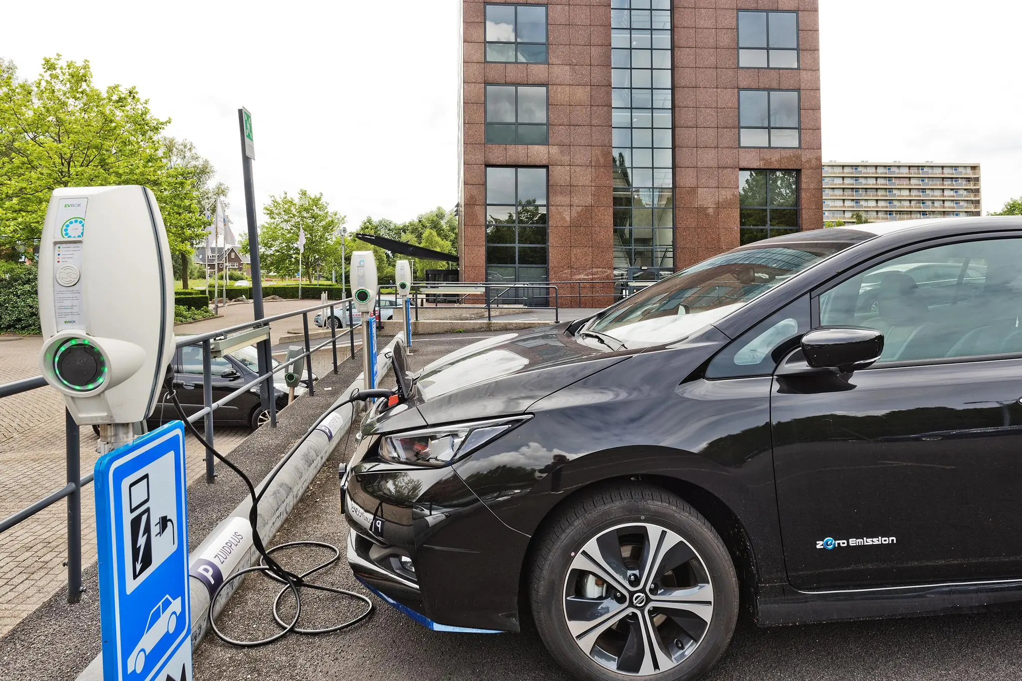 Zwarte elektrische auto laadt op bij een laadpaal op de Prof. W.H. Keesomlaan, naast een modern kantoorgebouw.