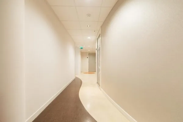 Licht gebogen gang met strakke witte muren en een golvend patroon op de vloer in zorginstelling Middenburcht.