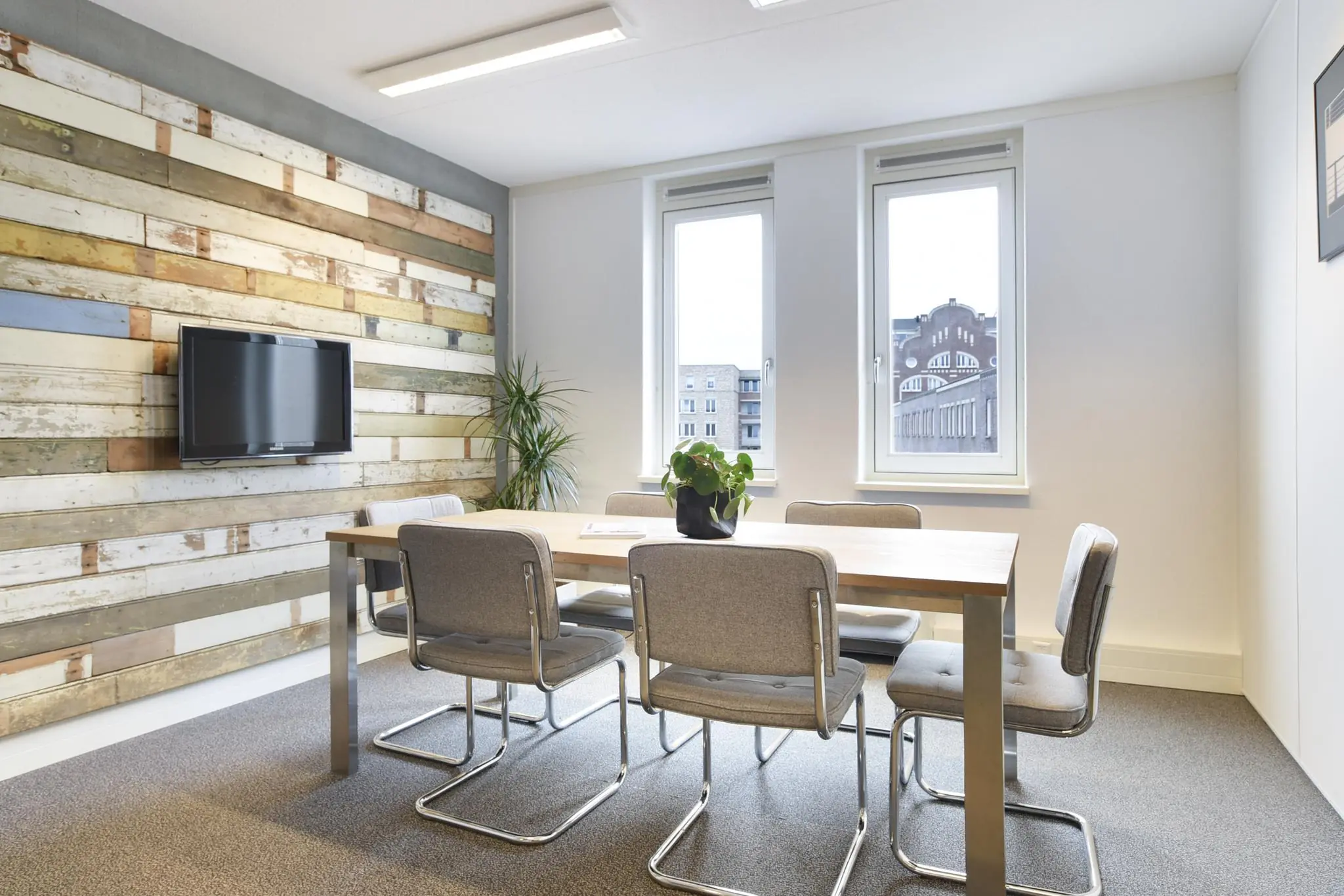Vergaderruimte met houten wand, moderne grijze stoelen, houten tafel en uitzicht op het Middenburcht-gebouw.