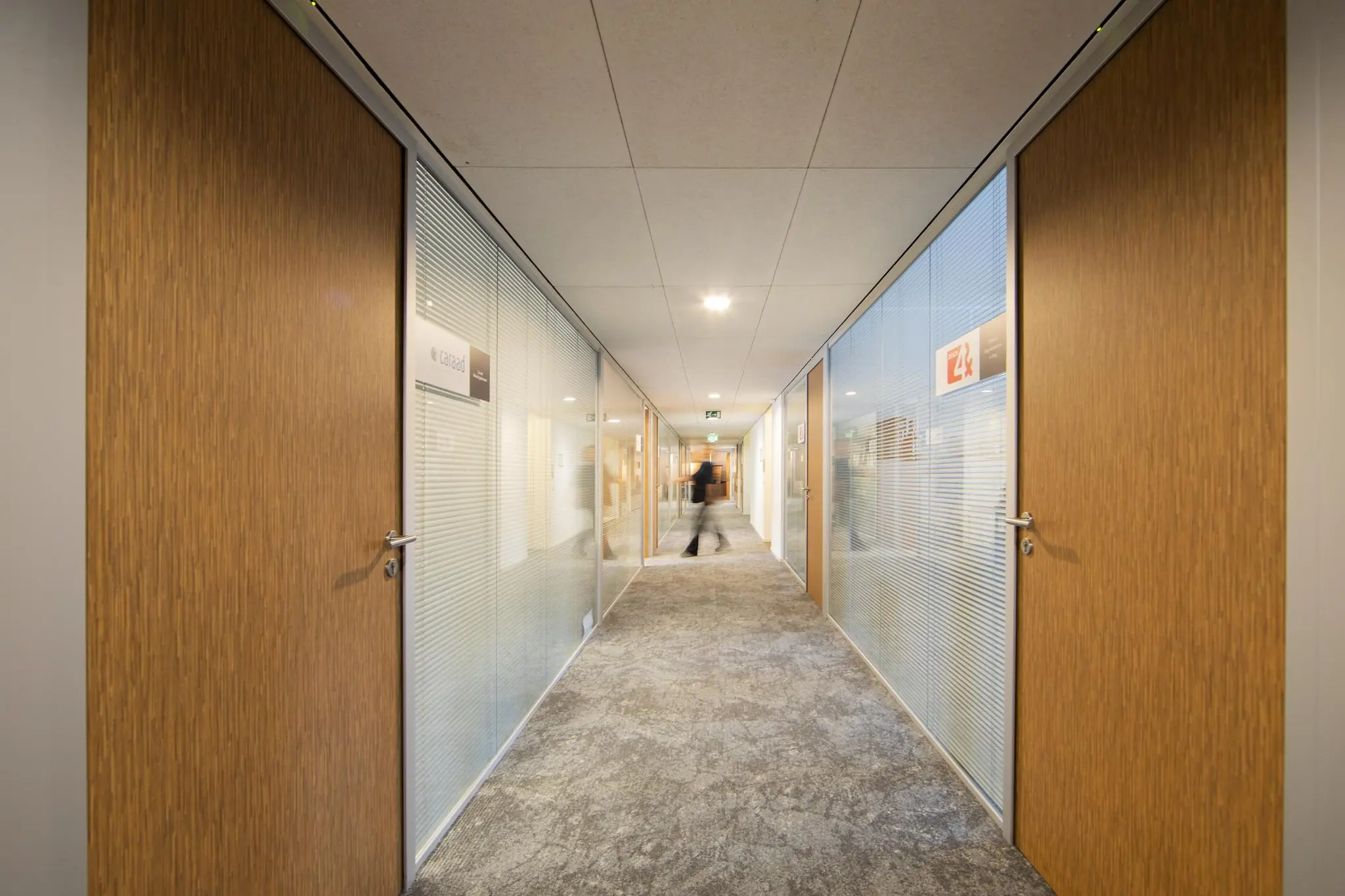 Verlichtte kantoorhal van kantoorgebouw Middenburcht met houten deuren en glazen wanden.