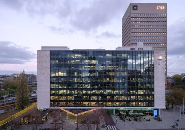 Modern kantoorgebouw aan het Hofplein in Rotterdam met een glazen gevel en oplichtende klok op de toren.