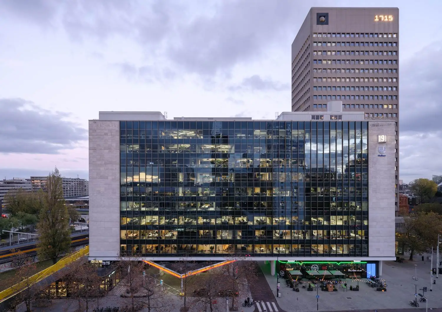 Modern kantoorgebouw aan het Hofplein in Rotterdam met een glazen gevel en oplichtende klok op de toren.