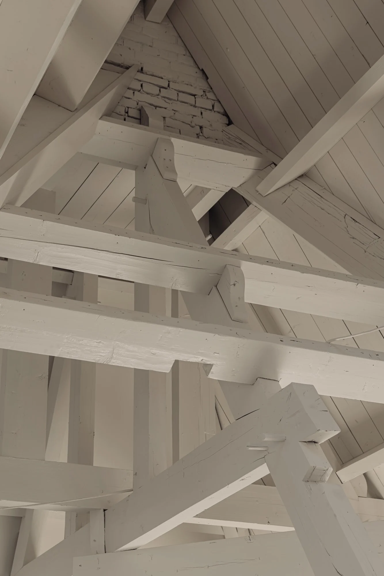 Houten dakconstructie met witgeschilderde balken en zichtbare bakstenen muur aan de Leidseweg.