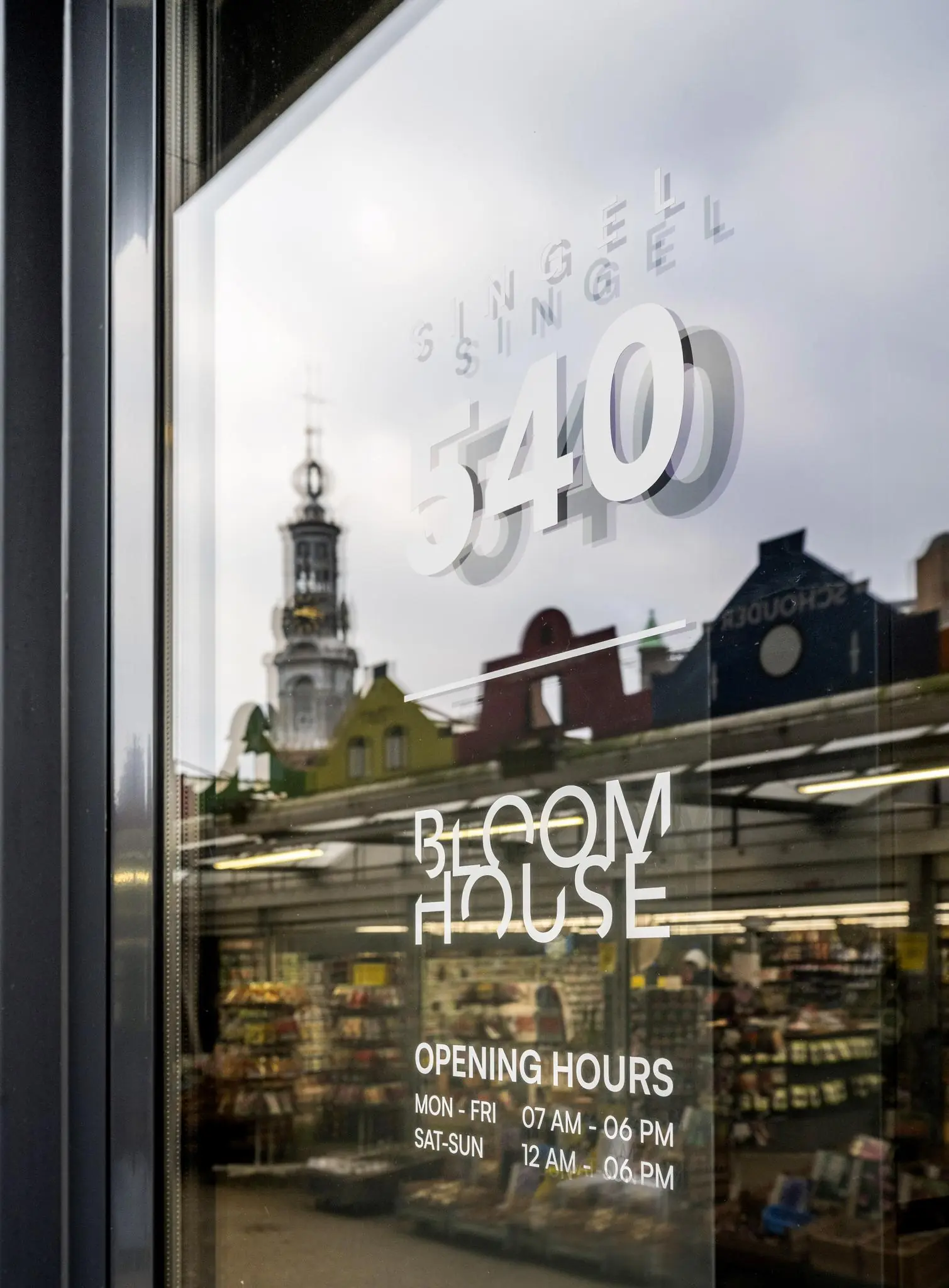 Glasdeur met het adres Singel 540 en de naam Bloom House, met daarachter een bloemenwinkel en de Munttoren weerspiegeld in het raam.