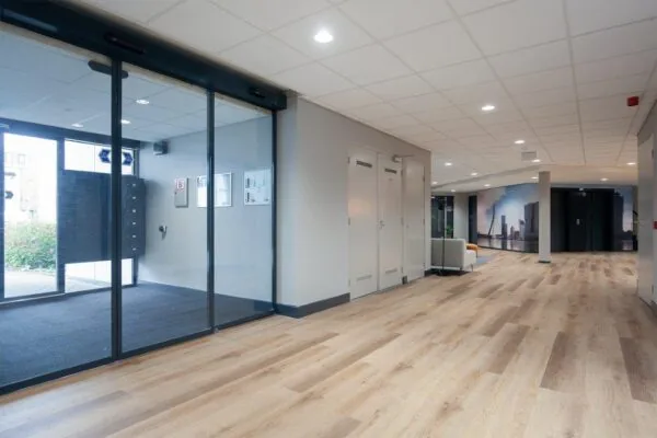Moderne en lichte entreehal van een bedrijfsverzamelgebouw aan de Cypresbaan met houten vloer en glazen schuifdeuren.