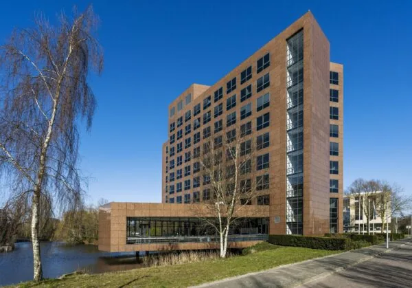 Modern kantoorgebouw aan de Prof. W.H. Keesomlaan met roodbruine gevel en grote ramen, gelegen aan het water.