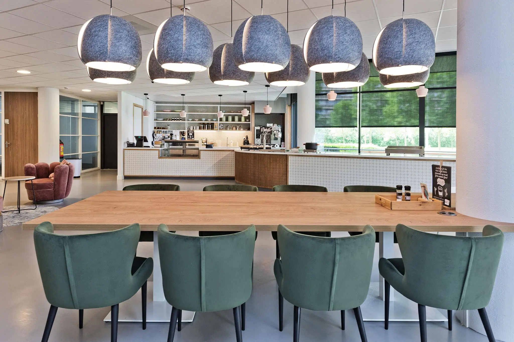 Moderne, open kantoorkantine met lange houten tafel, groene stoelen en hanglampen, aan de Prof. W.H. Keesomlaan.
