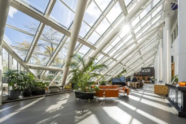 Lichte en moderne serre met schuine glazen wanden aan de Johan Huizingalaan, ingericht met planten, zitplaatsen en een piano.