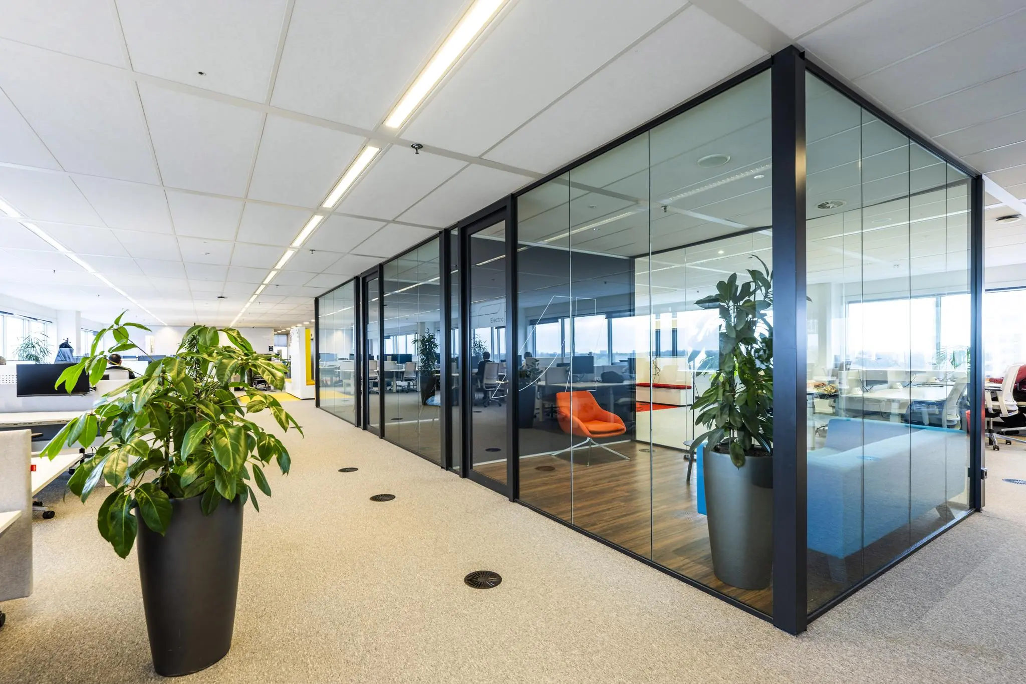 Modern kantoorinterieur aan de Johan Huizingalaan met glazen vergaderruimtes, felgekleurde meubels en grote planten.