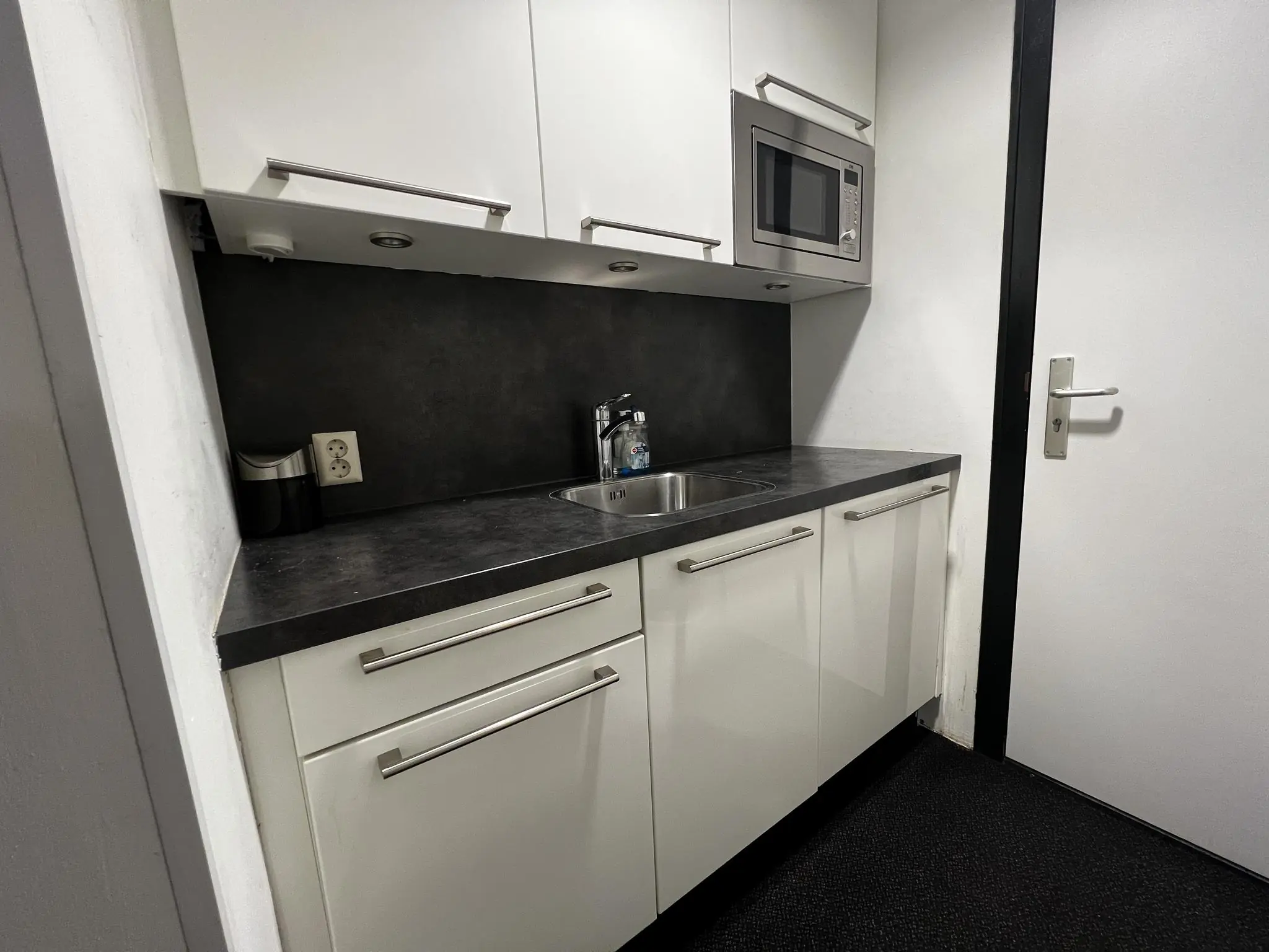 Kleine moderne kitchenette met witte kasten, een ingebouwde magnetron en een zwart aanrechtblad aan de Vreeswijksestraatweg.