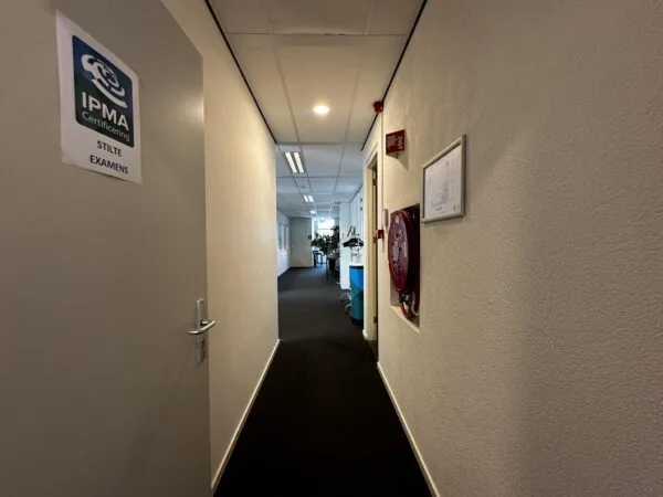 Gang van een kantoorpand aan de Vreeswijksestraatweg met een open deur naar een stilteruimte voor IPMA-examens.
