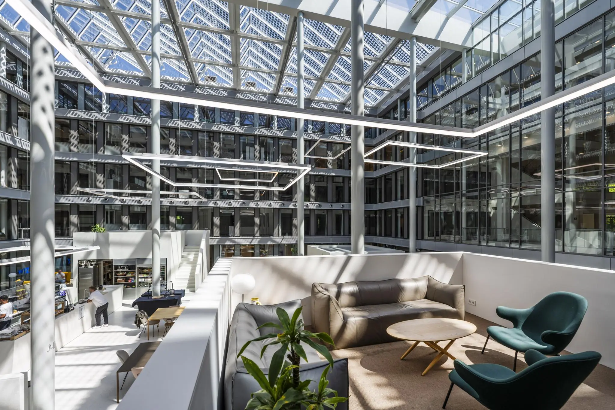 Modern atrium van een kantoorpand aan de Mr. Treublaan met glazen dak, zithoeken en een binnencafé.