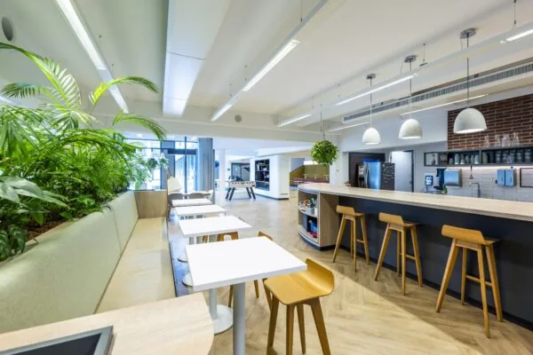 Moderne en lichte bedrijfskantine aan de Mr. Treublaan met zitgedeelte, bar, planten en een voetbaltafel op de achtergrond.