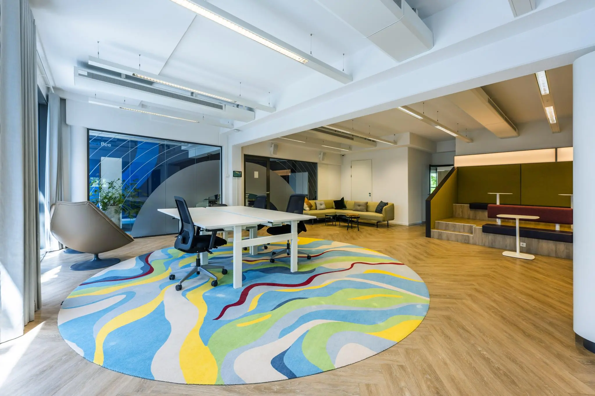 Modern kantoorinterieur aan de Mr. Treublaan met kleurrijk vloerkleed, flexwerkplekken en een zithoek.