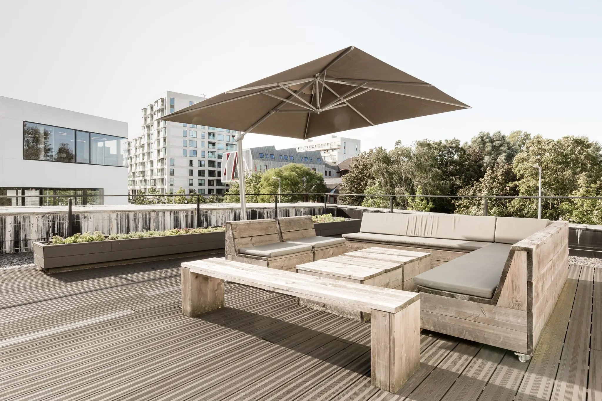 Dakterras aan de Fred. Roeskestraat met houten loungeset, parasol en uitzicht op omliggende moderne gebouwen.
