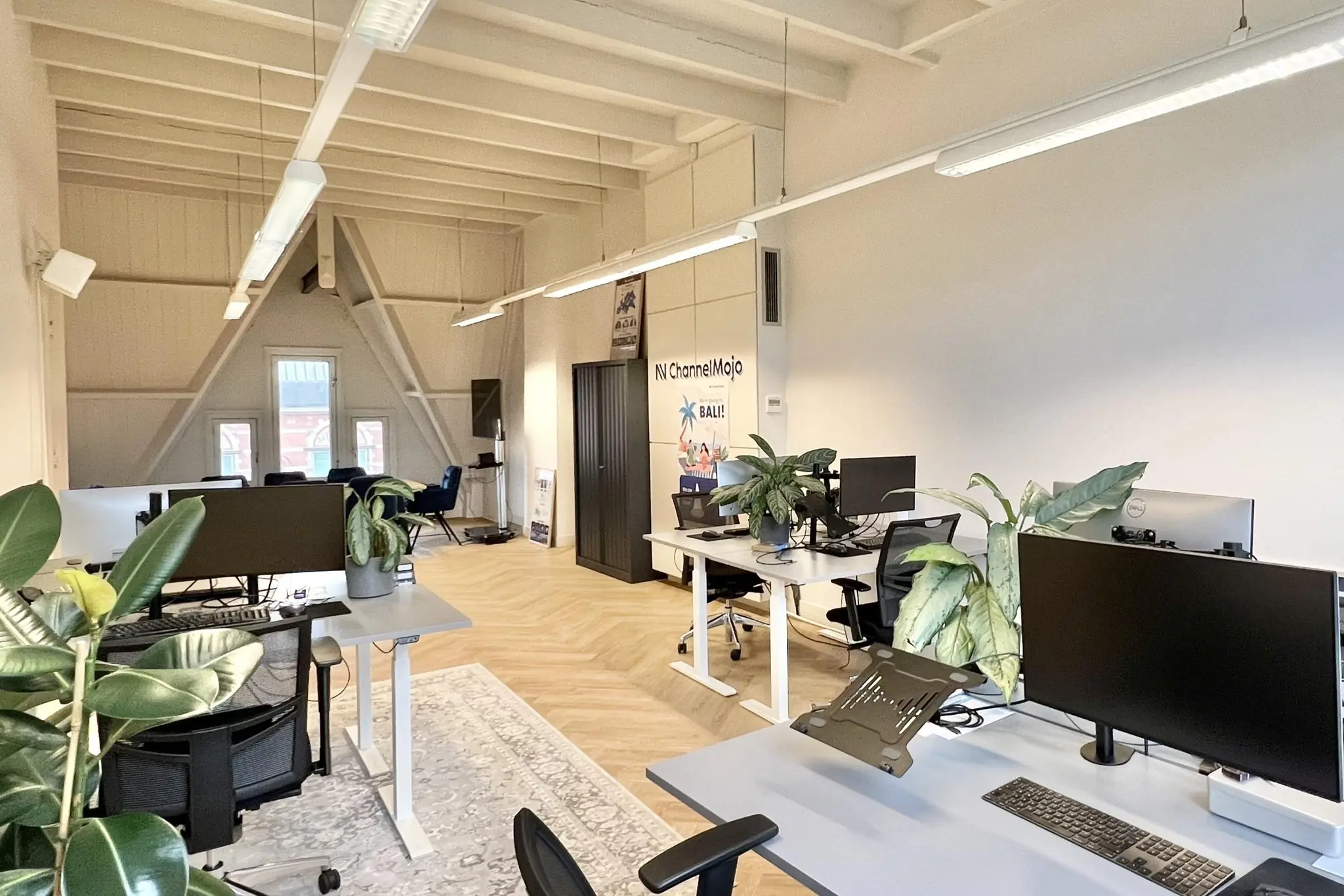 Modern kantoorinterieur aan de Paulus Potterstraat met werkplekken, planten en een hoog schuin plafond.