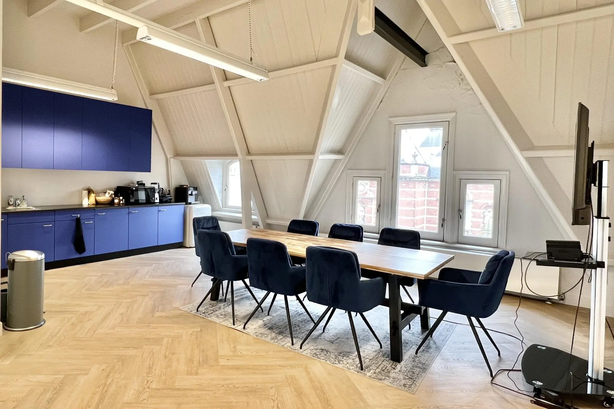Moderne vergaderruimte aan de Paulus Potterstraat met houten tafel, fluwelen stoelen, keukenblok en groot beeldscherm.
