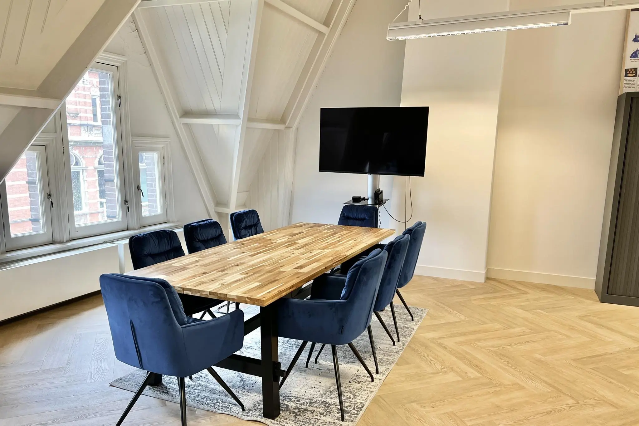 Vergaderruimte aan de Paulus Potterstraat met houten tafel, blauwe stoelen en flatscreen-tv aan de wand.
