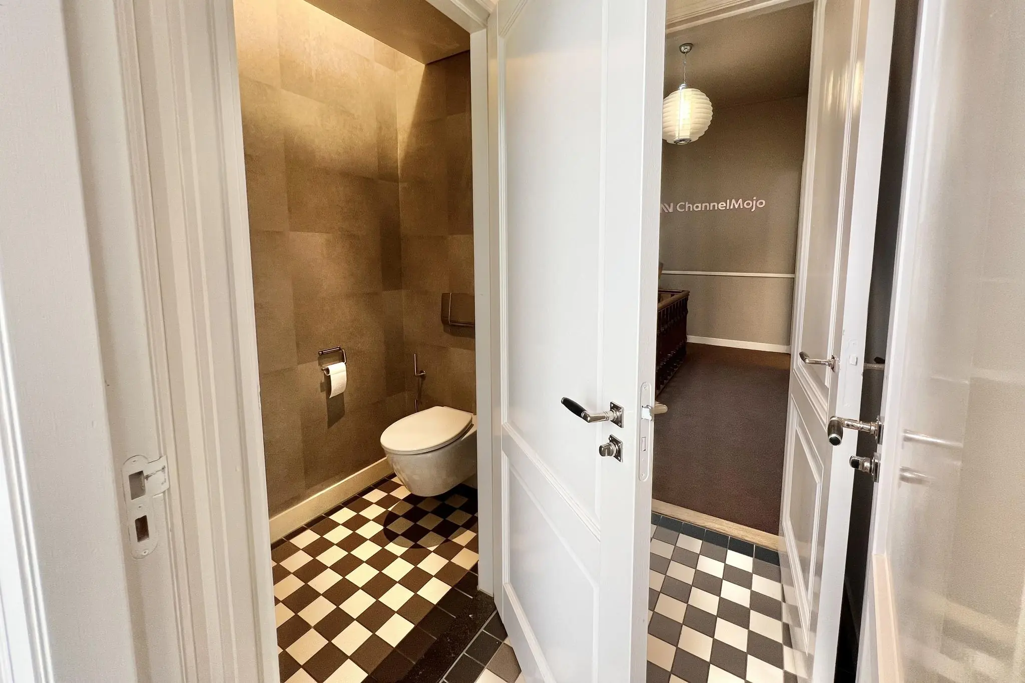 Binnenzicht van een toiletruimte met zwart-wit geblokte vloertegels en openstaande witte deur in een pand aan de Paulus Potterstraat.