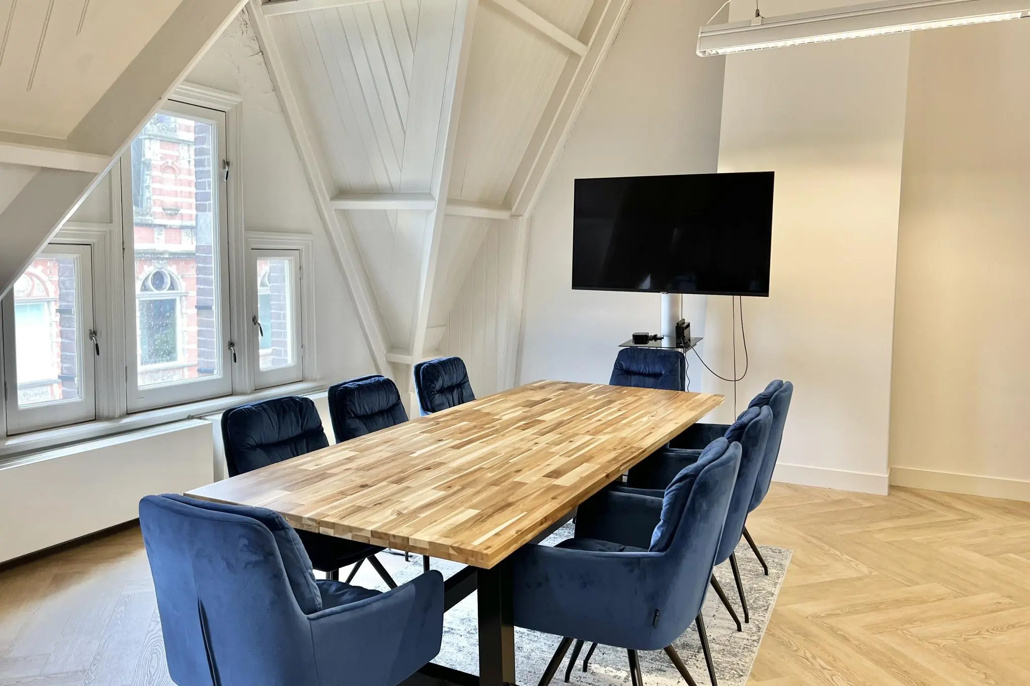 Vergaderruimte met een houten tafel, acht blauwe stoelen, een flatscreen-tv aan de muur en zicht op de Paulus Potterstraat.